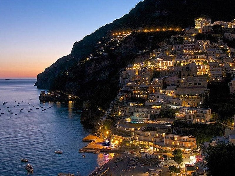Positano lit up at night above the dark sea